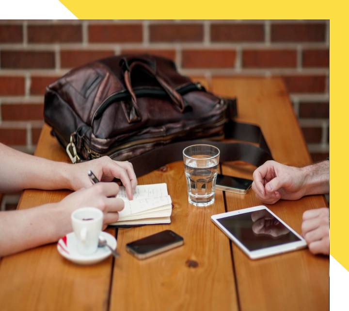 A group of people sitting at a table with bags and cups.