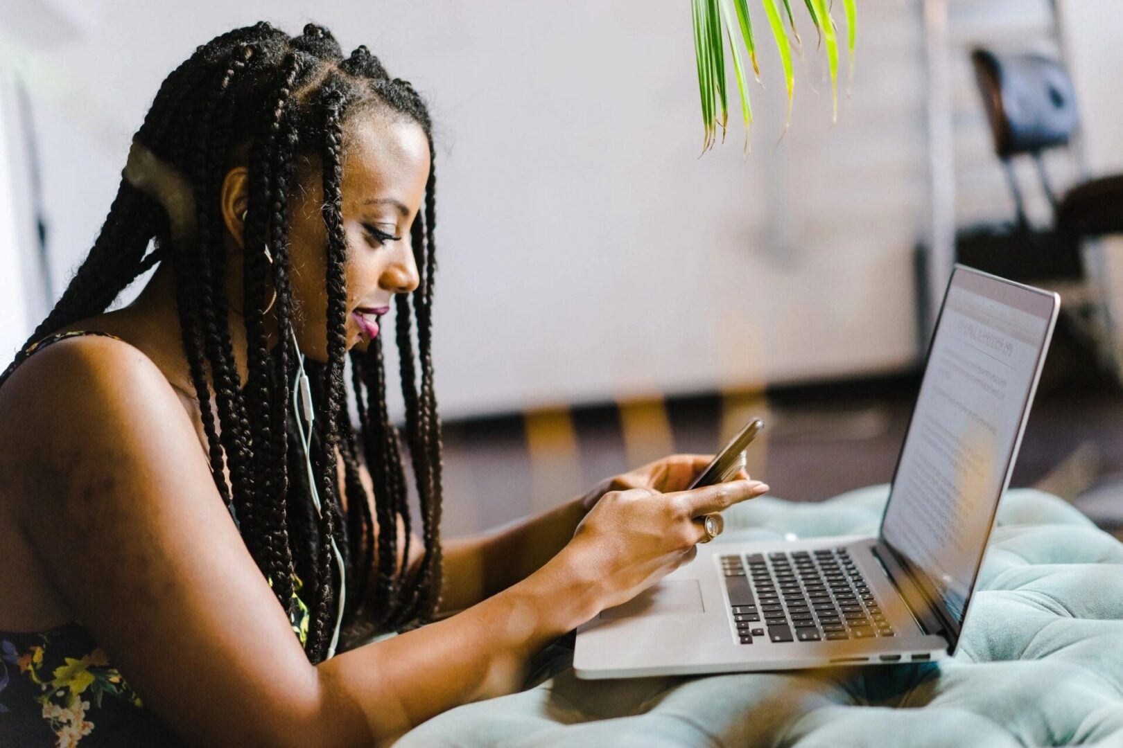 A woman is looking at her phone while using a laptop.